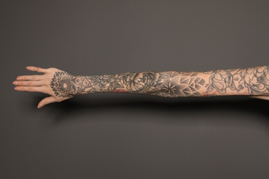 Woman with colorful tattoos on arm against dark grey background, closeup