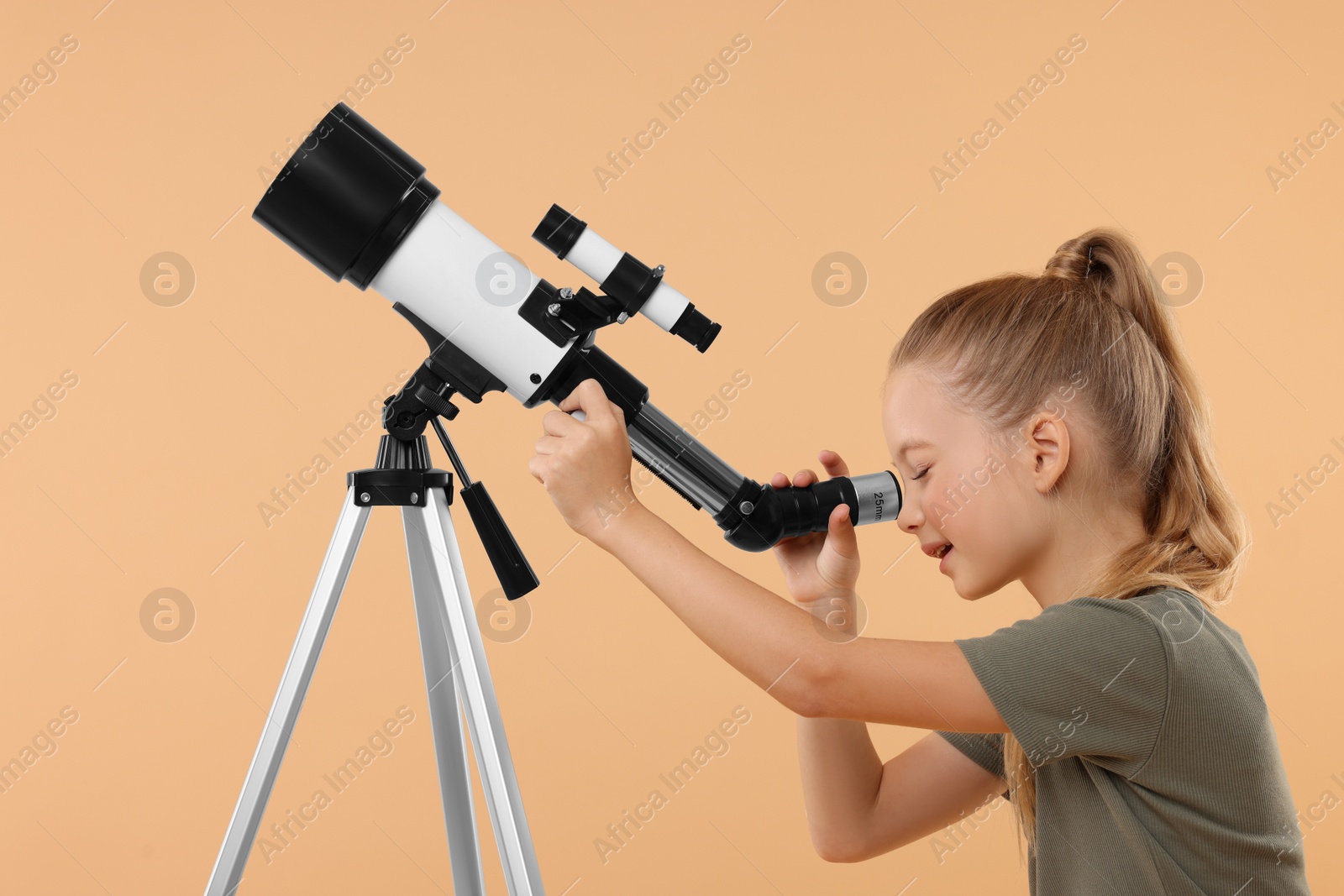 Photo of Little girl looking at stars through telescope on beige background