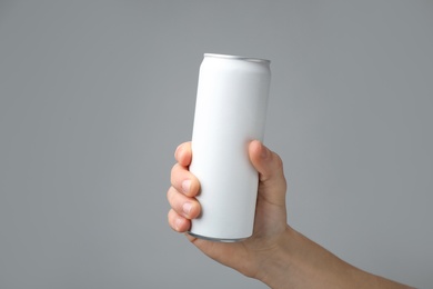 Man holding aluminum can with beverage on grey background, closeup. Space for design