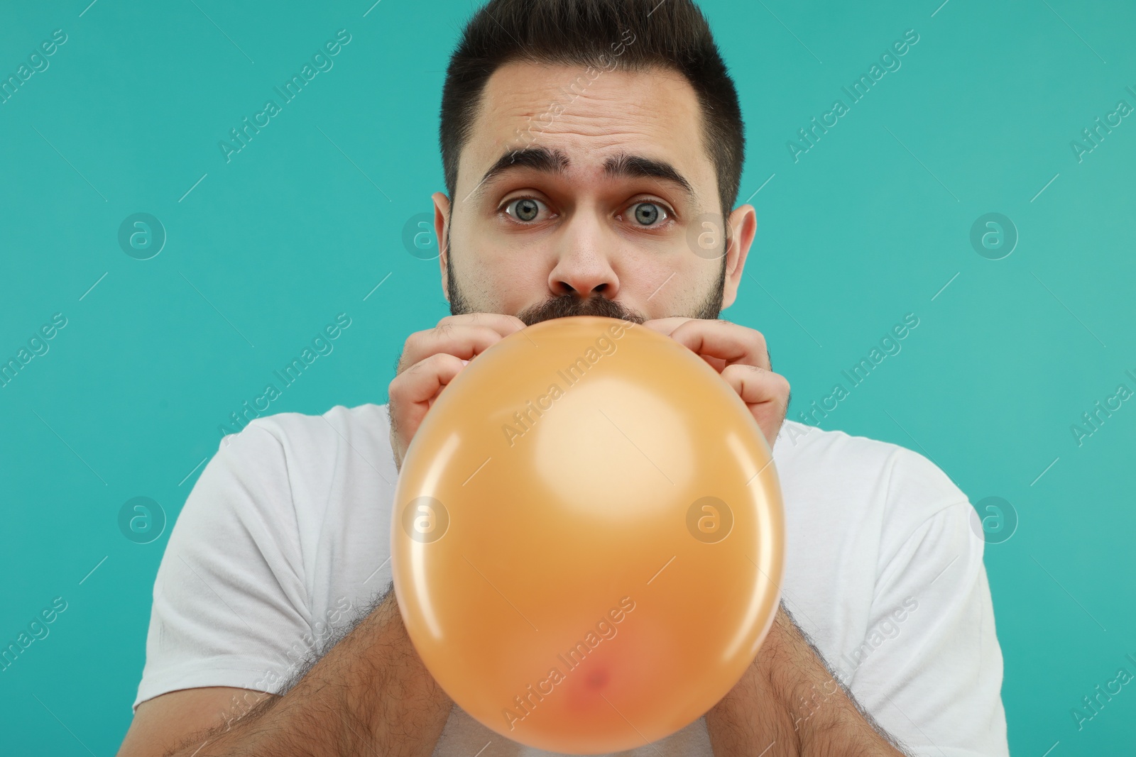 Photo of Man inflating bright balloon on turquoise background