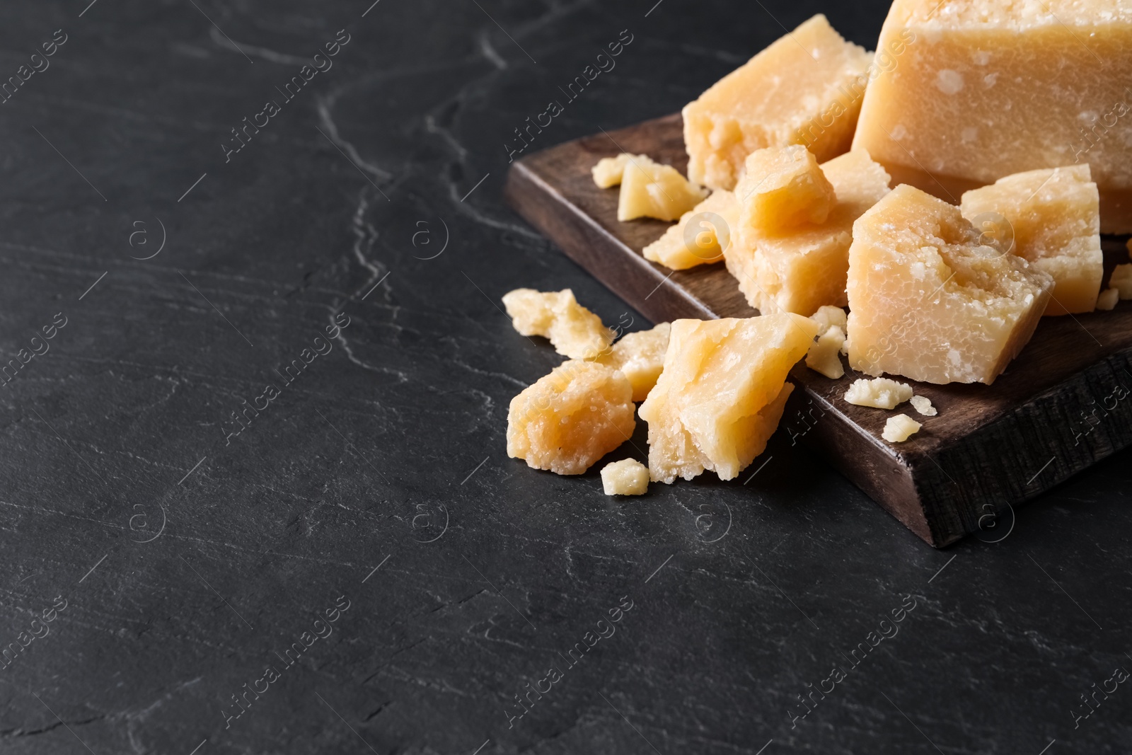 Photo of Pieces of delicious parmesan cheese on black table. Space for text