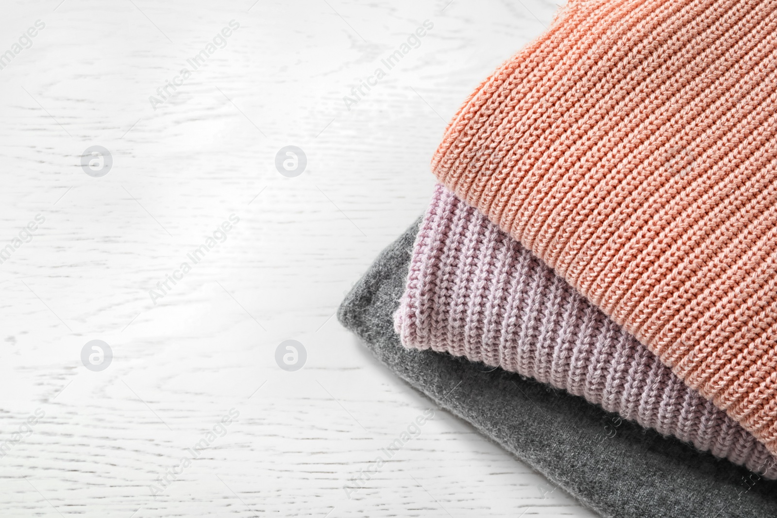 Photo of Stack of warm knitted clothes on light background