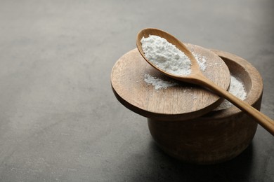 Photo of Baking powder in bowl and spoon on grey textured table, space for text