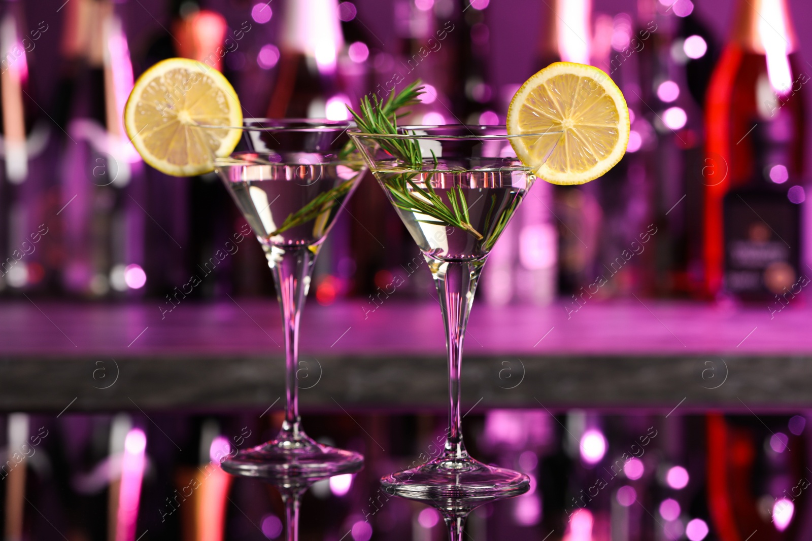 Photo of Martini glasses of refreshing cocktail, lemon slices and rosemary on mirror surface
