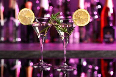 Martini glasses of refreshing cocktail, lemon slices and rosemary on mirror surface