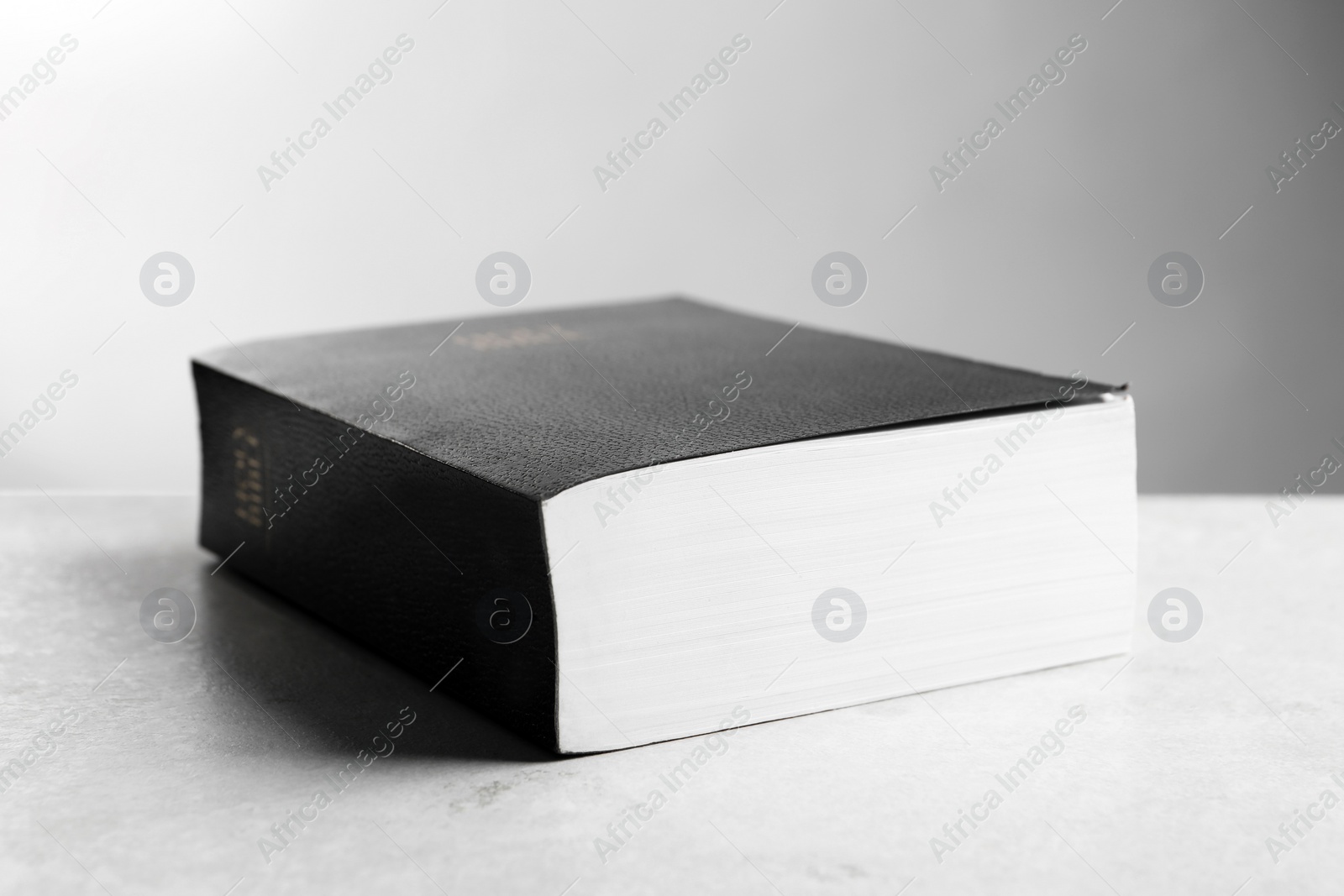 Photo of Bible with black cover on light gray table, closeup. Christian religious book