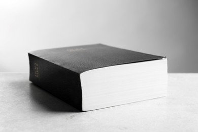 Bible with black cover on light gray table, closeup. Christian religious book