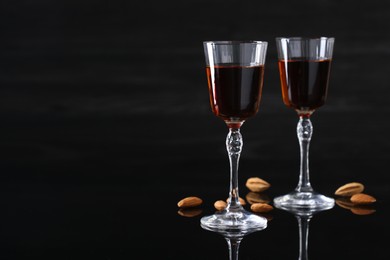 Liqueur glasses with tasty amaretto and almonds on black table, space for text