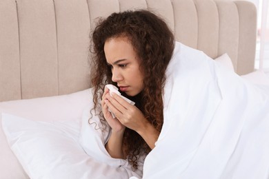 Sick African American woman with tissue in bed at home