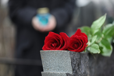 Photo of Red roses on grey granite tombstone outdoors. Funeral ceremony
