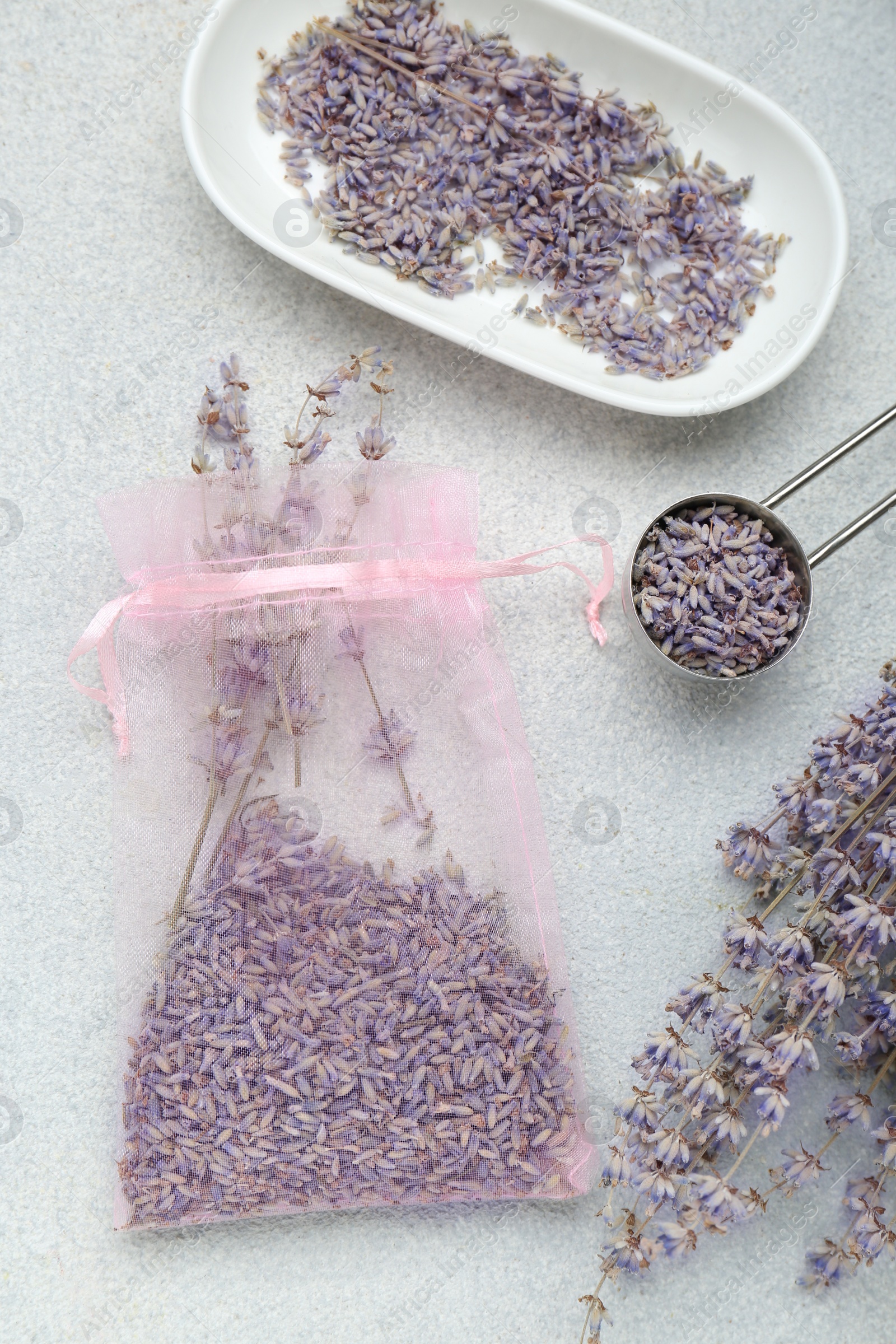Photo of Scented sachet and dried lavender flowers on light gray textured table, flat lay