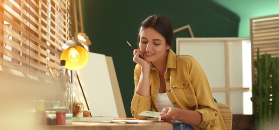 Image of Young woman drawing on paper at table indoors. Banner design