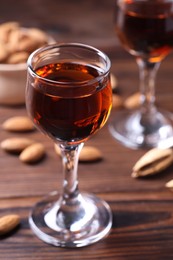 Photo of Liqueur glass with tasty amaretto and almonds on wooden table, closeup