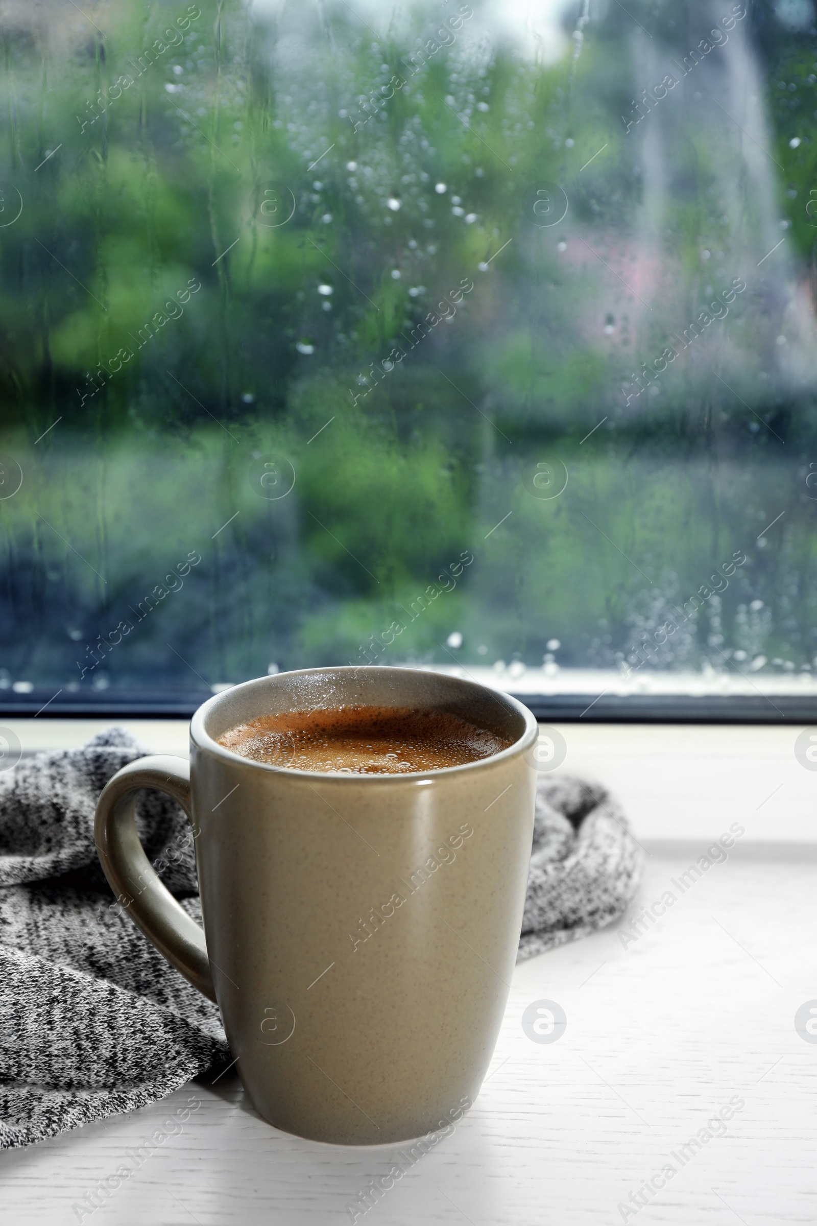 Photo of Cup of hot drink on window sill against glass with rain drops, space for text