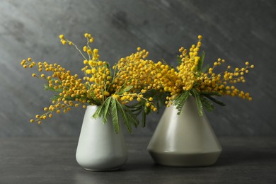 Photo of Beautiful mimosa flowers in vases on black background