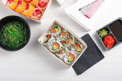 Photo of Food delivery. Paper boxes with delicious sushi rolls on white wooden table