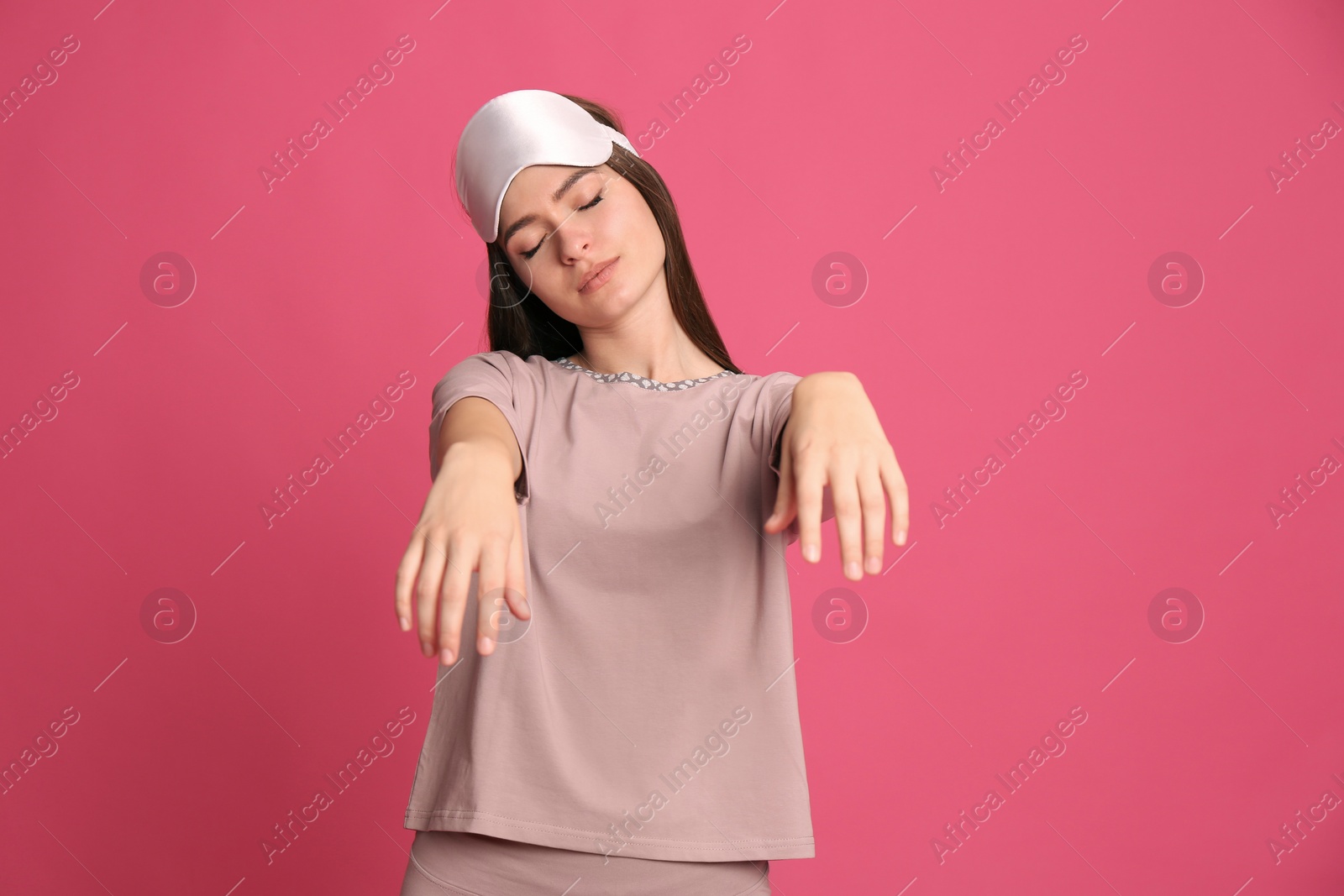 Photo of Young woman wearing pajamas and mask in sleepwalking state on pink background