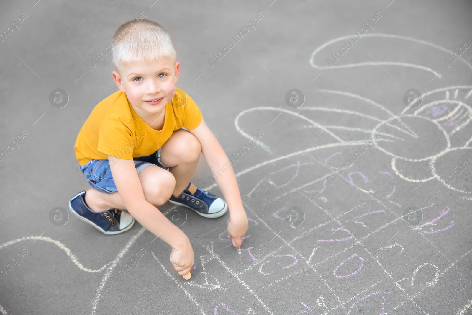 Photo of Little child drawing bunny with colorful chalk on asphalt