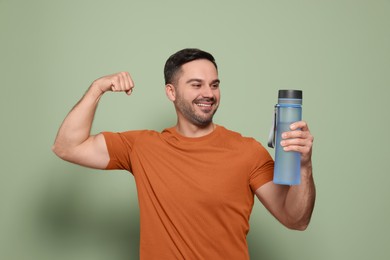 Happy man holding transparent bottle of water and showing arm on light green background