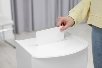 Photo of Woman putting her vote into ballot box on blurred background, closeup