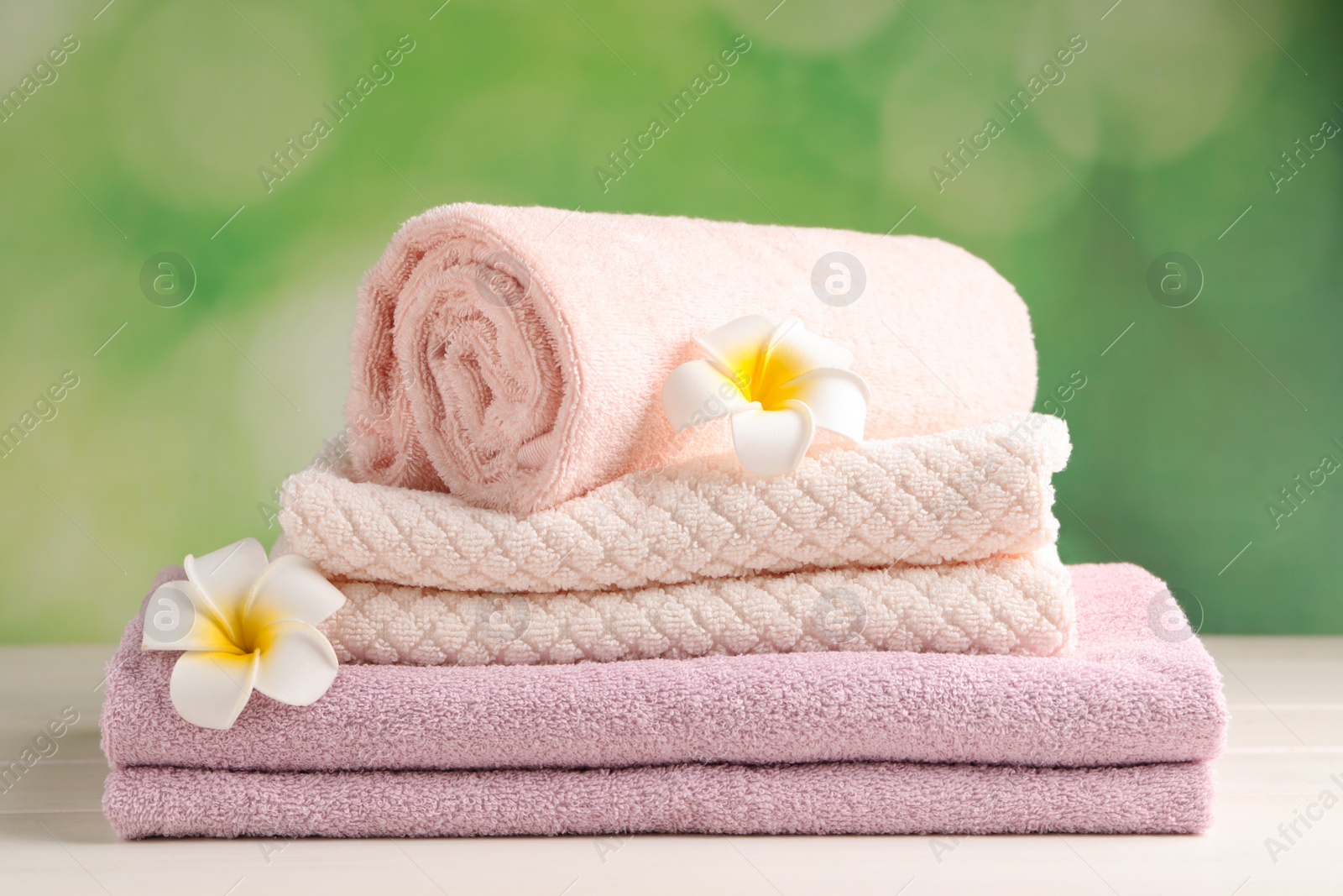 Photo of Soft folded towels and plumeria flowers on white wooden table