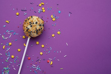 Delicious confectionery. Sweet cake pop and sprinkles on purple background, flat lay. Space for text