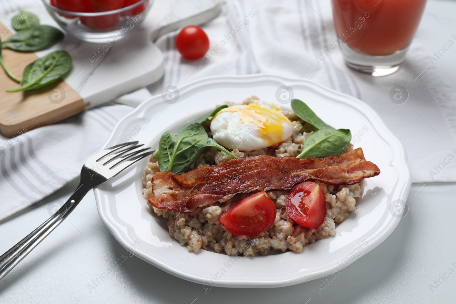 Photo of Delicious boiled oatmeal with poached egg, bacon and tomato served on white table, closeup