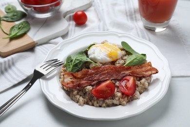 Delicious boiled oatmeal with poached egg, bacon and tomato served on white table, closeup