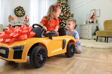 Cute little boy pushing toy car with his sister in room decorated for Christmas