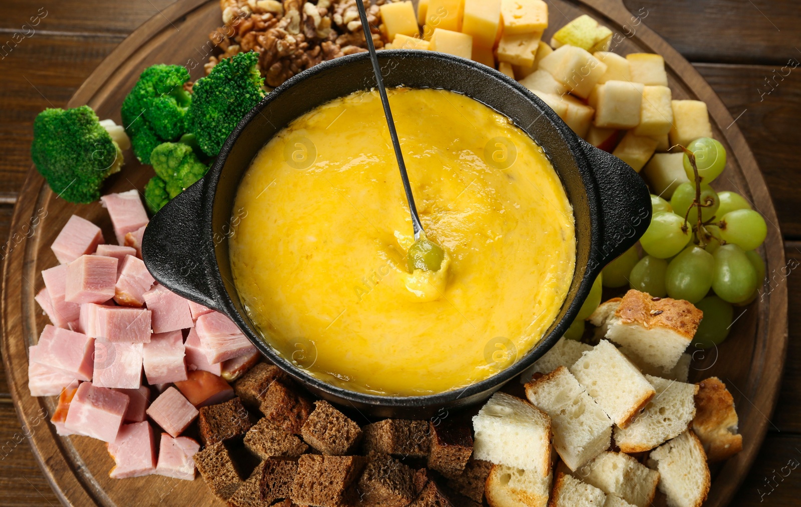 Photo of Fondue pot with melted cheese and different products on wooden table, above view