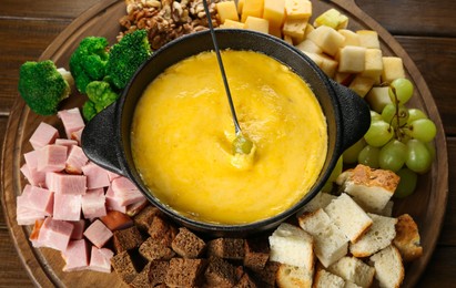 Photo of Fondue pot with melted cheese and different products on wooden table, above view