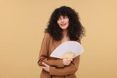 Happy woman holding hand fan on beige background