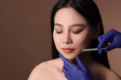 Photo of Woman getting lip injection on brown background