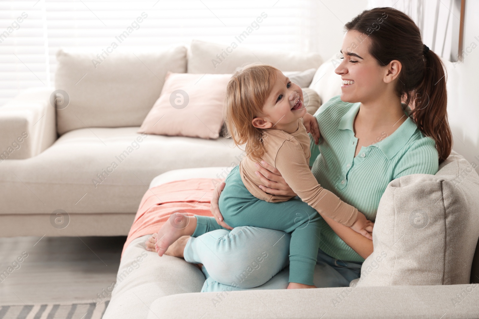 Photo of Mother with her cute little daughter on sofa at home, space for text