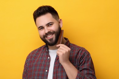 Photo of Handsome young man combing beard on yellow background