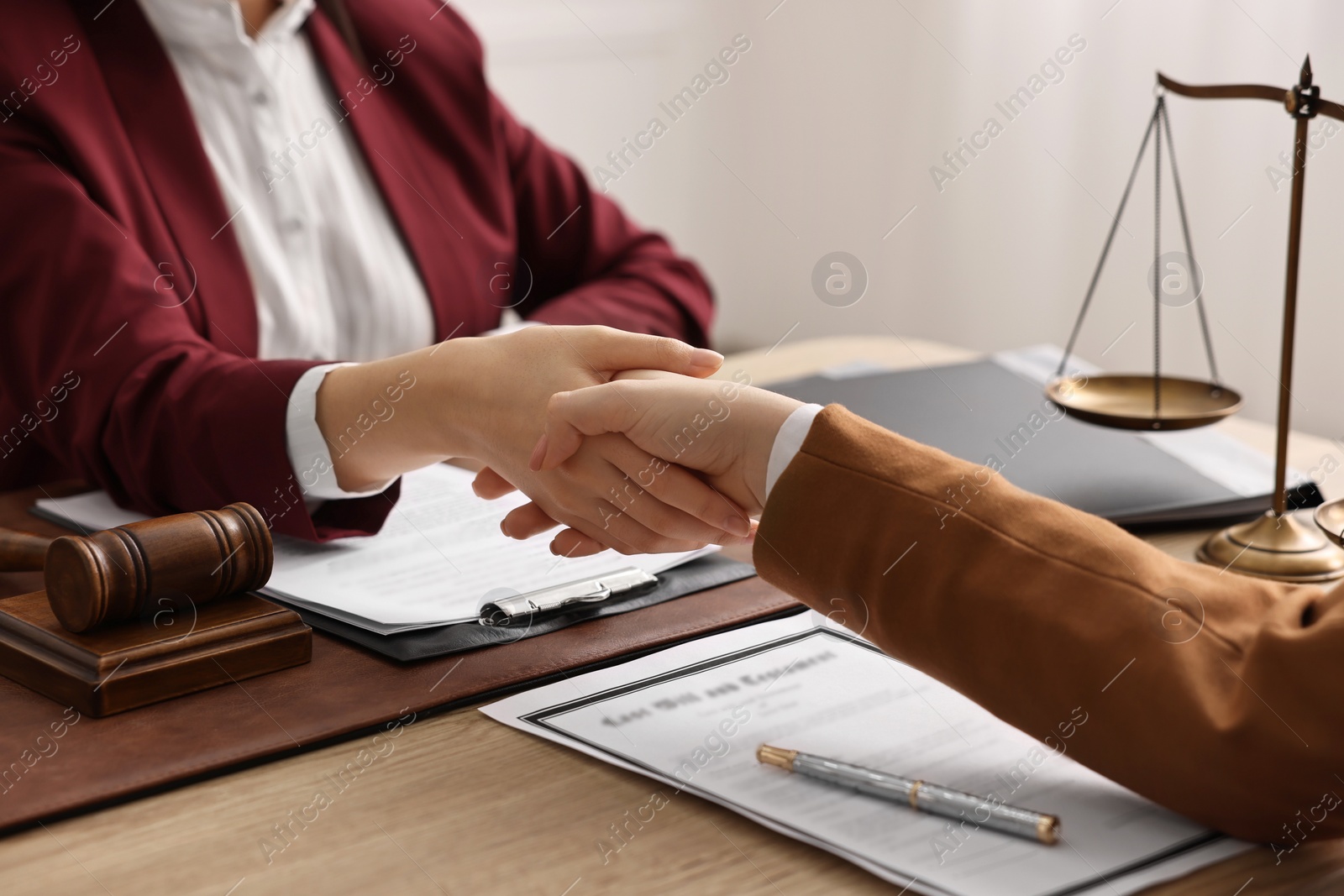 Photo of Notary shaking hands with client at wooden table in office, closeup