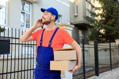 Photo of Courier with parcels talking on smartphone outdoors. Order delivery