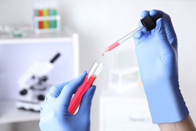 Assistant dripping sample into test tube at chemistry laboratory, closeup