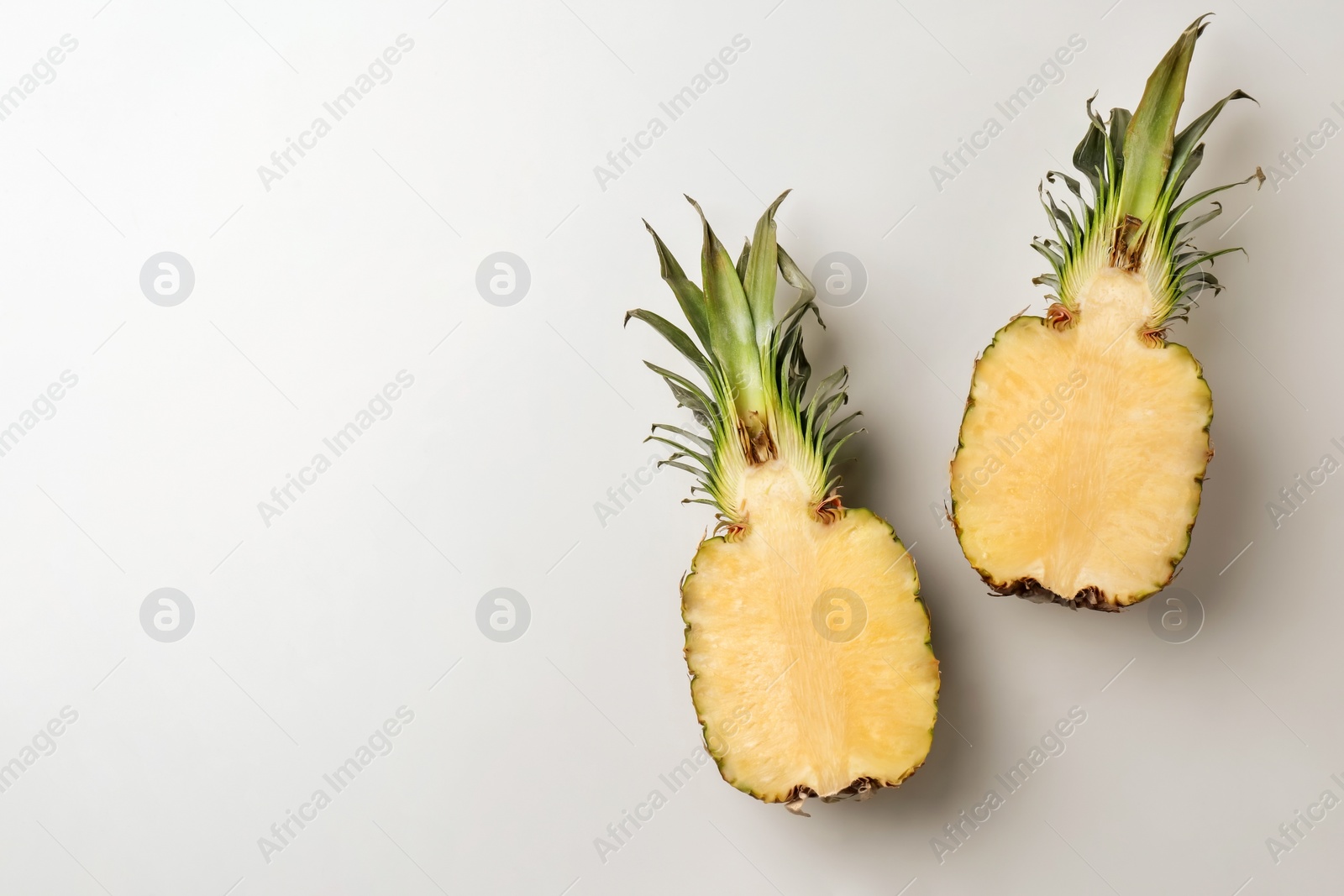 Photo of Fresh pineapple halves on light background, top view