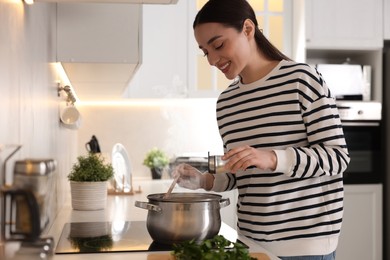 Photo of Smiling woman adding spices into pot with soup in kitchen