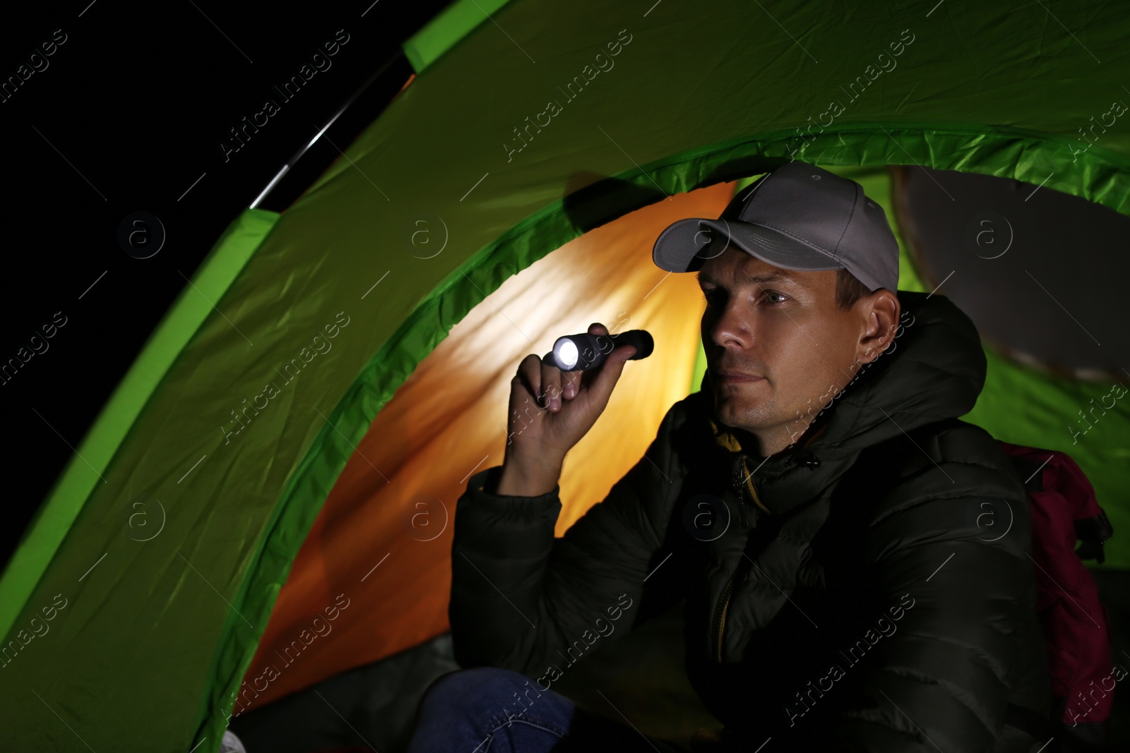 Photo of Man with flashlight sitting in tent at night