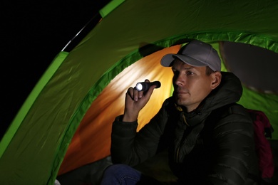Photo of Man with flashlight sitting in tent at night