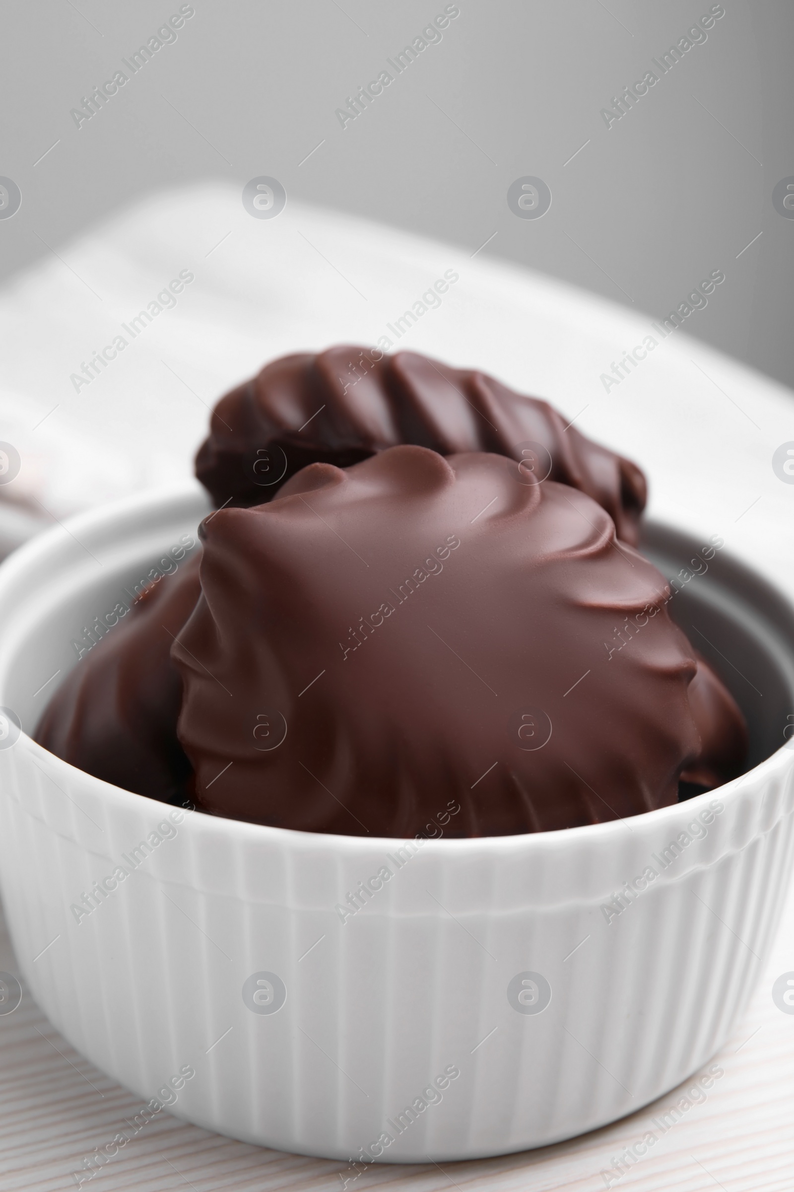 Photo of Delicious chocolate covered zephyrs in bowl on white wooden table, closeup