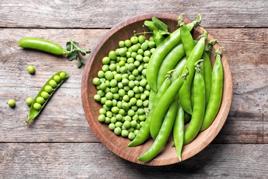 Photo of Bowl with delicious fresh green peas on wooden table, top view