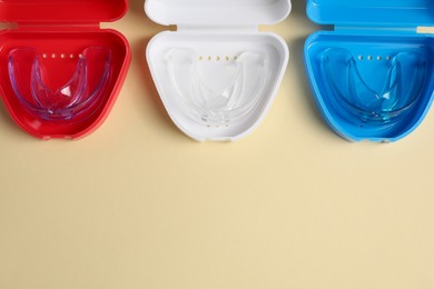 Transparent dental mouth guards in containers on beige background, flat lay with space for text. Bite correction
