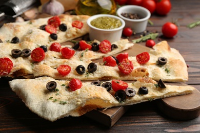 Photo of Focaccia bread with olives and tomatoes on wooden table, closeup