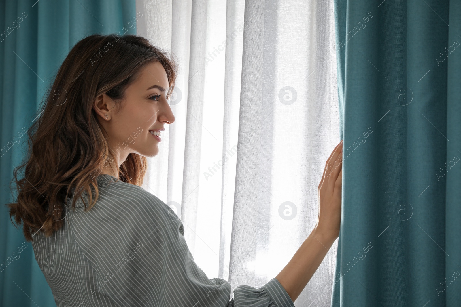 Photo of Woman opening window curtains at home in morning