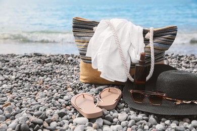 Photo of Beautiful hat with sunglasses, bag and flip flops near sea on pebble beach