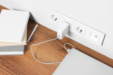 Photo of Modern laptop charging from power socket on wooden table