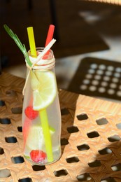 Photo of Refreshing tasty lemonade served in glass bottle on wicker surface